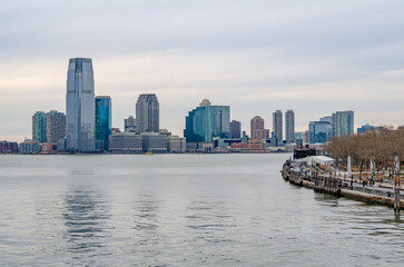Fototapeta premium Jersey City, New Jersey with office skyscraper, Hudson river and Manhattan river bank in forefront, during winter evening with overcast, horizontal