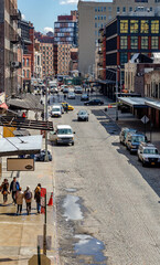 Obraz premium Chelsea City Street with people walking on sidewalk and traffic on the street, lots of cars parked on the street, aerial view during sunny winter day, puddle on the street, vertical