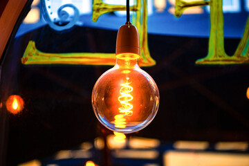 A large round Incandescent light bulb yellow warm color lamp hangs on the ceiling in a cafe