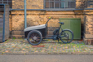 A tricycle cargo family bike with box for the transport of children stands on a street in old town. Copenhagen, Denmark