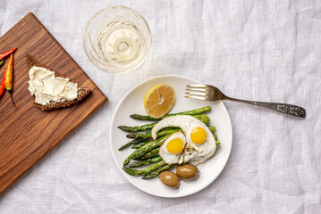 Fried eggs with asparagus and olives. Top View. Next to a glass of white wine 