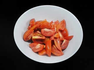 Top view of tomatoes sliced in white bowl isolated on black background (Solanum lycopersicum var. cerasiforme), Ready to eat or cooking