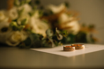 Two golden wedding rings and pink flowers on white background. Vertically framed shot.