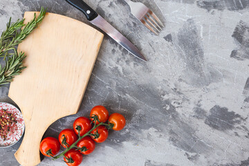 Obraz na płótnie Canvas wooden cutting board with cherry tomatoes and rosemary on a concrete background