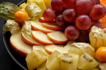 Sliced fruits on a plate, dessert. On a dark background.