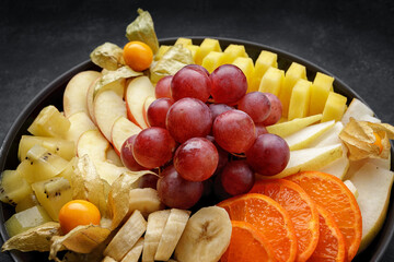 Sliced fruits on a plate, dessert. On a dark background.
