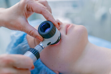 the doctor looks at the patient's skin under a dermatoscope 