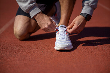 Runner man tying shoelace in the stadium, cross training workout. Sporty male training outside