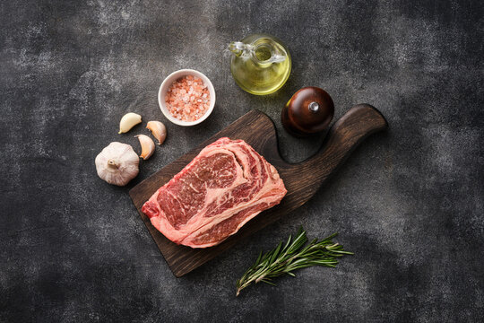 Raw ribeye steak on a wooden board. Preparing raw beef steak for barbecue grill.