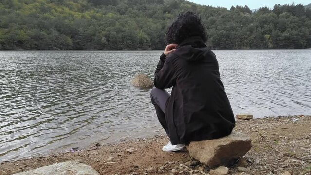Young woman, teen with the hands on her bowed head sitting sadly and loney on the lake shore. Depression and anxiety concept