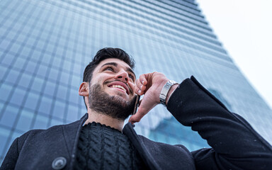 low angle view of a young handsome businessman using smartphone, background of a skyscraper of a...