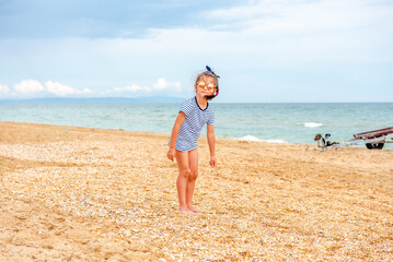 little charming girl 5-7 years old in a striped t-shirt happily plays on the beach on a sunny day on vacation 