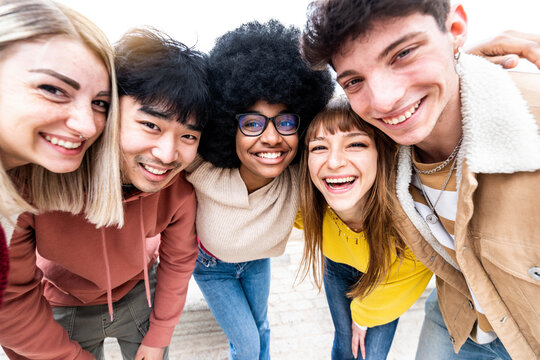 Multiracial group of best friends taking self photo smiling at camera - Happy mixed race teens having fun hanging out - Community of young people hugging together - Youth and friendship concept