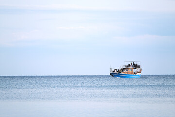 Obraz premium Blue boat with people in the sea in the distance on the horizon