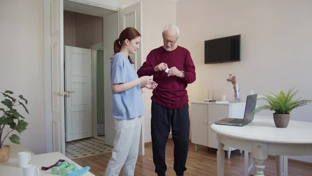 A woman helps an elderly man put on wireless headphones before morning exercises