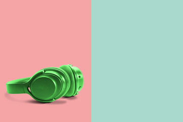 Computer headphones. Green headphones on a green-red pastel background. The concept of listening to music, creating audio, music. Computer work, abstraction and minimalist style.