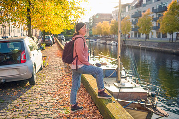 A black-haired young woman in casual clothes stands on the bank of a canal in the old town near a...
