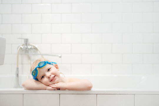 Portrait of a cute Child with white hair and underwater goggles on his head in a bathroom interior.