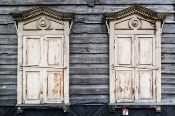 Two white carved windows in an old wooden gray house.