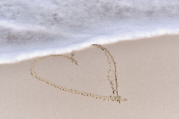 Contour of heart drawn on white sand of tropical beach.
