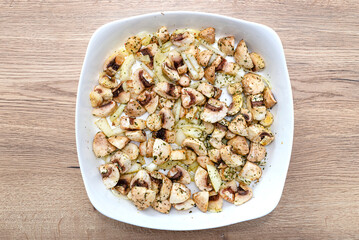 Raw sliced mushrooms lying in a plate with onions, prepared for baking, top view.