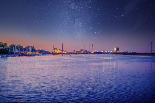 Sea bay with yachts, factory pipes and a processing factory against the background of the night sky and the stars of the milky way. Copenhagen, Denmark