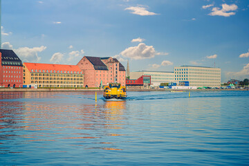 Yellow Copenhagen Harbour water Bus floats along the canal near the old warehouses. Copenhagen, Denmark - obrazy, fototapety, plakaty