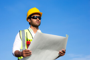 portrait of a man wind turbine engineer working and holding blueprint in yellow helmet standing in...