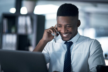 Its turning into one successful night. Shot of a young businessman talking on a cellphone while working on a laptop in an office at night.