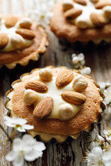 Close up view of mini tart with almond frangipane cream, white chocolate and nuts on wooden table decorated with spring flowers