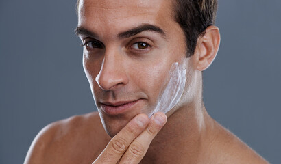 Even men like to be soft..... Studio shot of a handsome young man applying cream to his face.