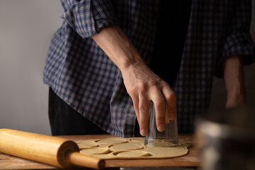 Dough rolling process. A man in a plaid shirt rolls out the dough with a rolling pin and cuts out the dough with a dumpling glass