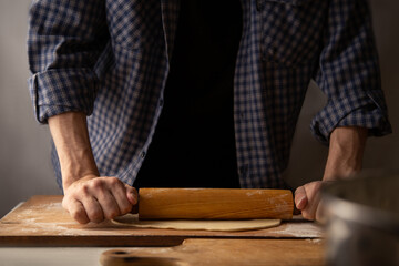 Dough rolling process. A man in a plaid shirt uses a rolling pin to roll out dough for making dumplings.