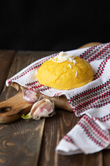 Traditional Moldovan cuisine. Hominy with cheese on a Moldovan towel and a wooden board and garlic on a dark background