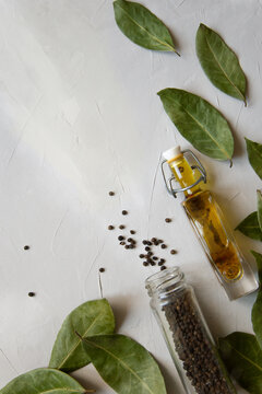 Top view of jar of black peppercorns, olive oil and bay leaf composition on light gray background
