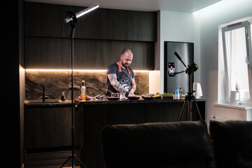 Tattooed chef preparing steak records online broadcasts. Live streaming concept