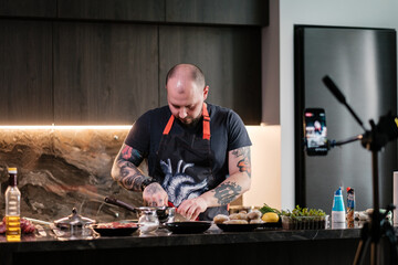 Tattooed chef preparing steak records online broadcasts.