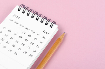 June 2022 desk calendar with wooden pencil on pink background.