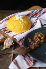 Traditional Moldovan cuisine. Hominy with cheese on a Moldovan towel and a wooden board, a plate with cracklings, a wooden spoon and garlic on a dark background