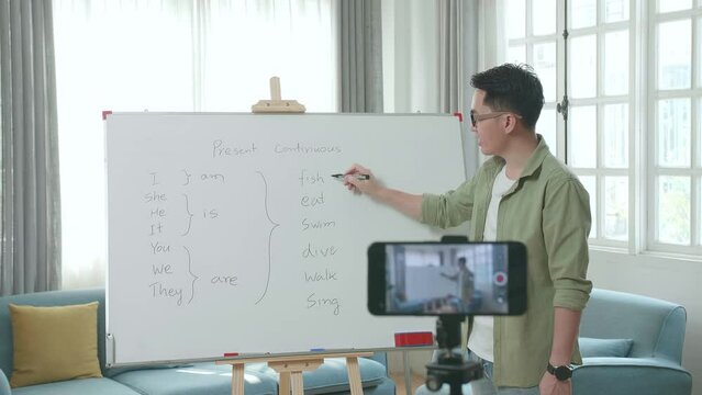 Asian Male Teacher With Glasses Shoots Video By Smartphone Camera While Teaching English At Home
