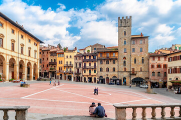 Couple sitting on the ground in the famous Piazza Grande square in the historic center of Arezzo, Italy