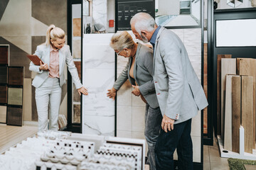 Senior couple are buying ceramic tiles and utensils for their home and female seller is helping...
