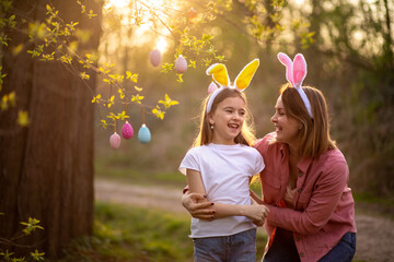 beautiful and happy mom and daughter in bunny ears decorate the tree with easter eggs. happy family celebrating easter