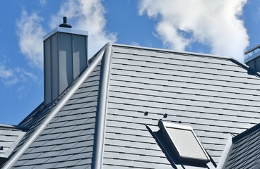 Modernes Ziegel- oder Metalldach mit Dachrinne, Dachfenster, Schneefang und Schornstein mit...