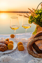 Romantic picnic at sunset by the sea, focus on glasses. Delicate bouquet of dried flowers and sweet snacks.
