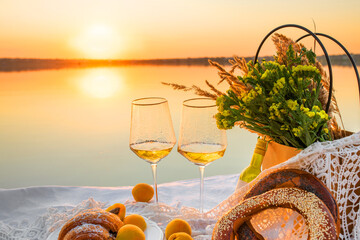 Romantic picnic at sunset by the sea, focus on glasses. Delicate bouquet of dried flowers and sweet snacks.