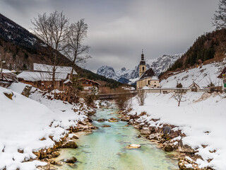 Bavarian Church with a ice cold river and the Berchtesgaden mountain chain at the background hidden by the winter clouds