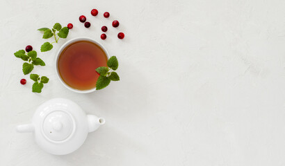tea in a cup brewed with cranberries, sea buckthorn and mint leaves, next to a white teapot, top view, tea drinking, breakfast, a healing drink for diseases