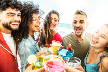 Happy multiracial friends cheering drinks in patio cocktail bar - Young people celebrating summertime party holding cocktail glasses outside - Summer vacations and lifestyle beverage concept