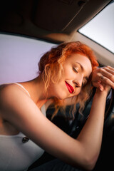 Beautiful redhead girl posing in the car at sunset